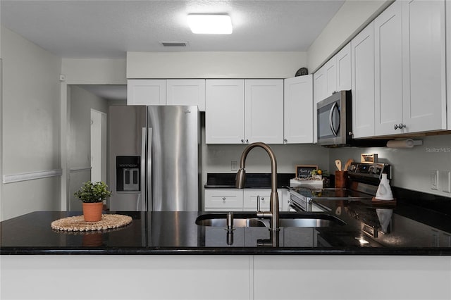 kitchen with white cabinets, sink, a textured ceiling, kitchen peninsula, and stainless steel appliances