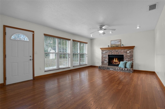 unfurnished living room with ceiling fan, wood-type flooring, a textured ceiling, and a brick fireplace