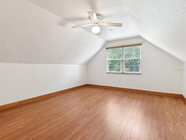 additional living space featuring vaulted ceiling, ceiling fan, light hardwood / wood-style flooring, and a textured ceiling