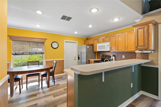 kitchen with light hardwood / wood-style flooring, kitchen peninsula, stainless steel appliances, backsplash, and a breakfast bar area