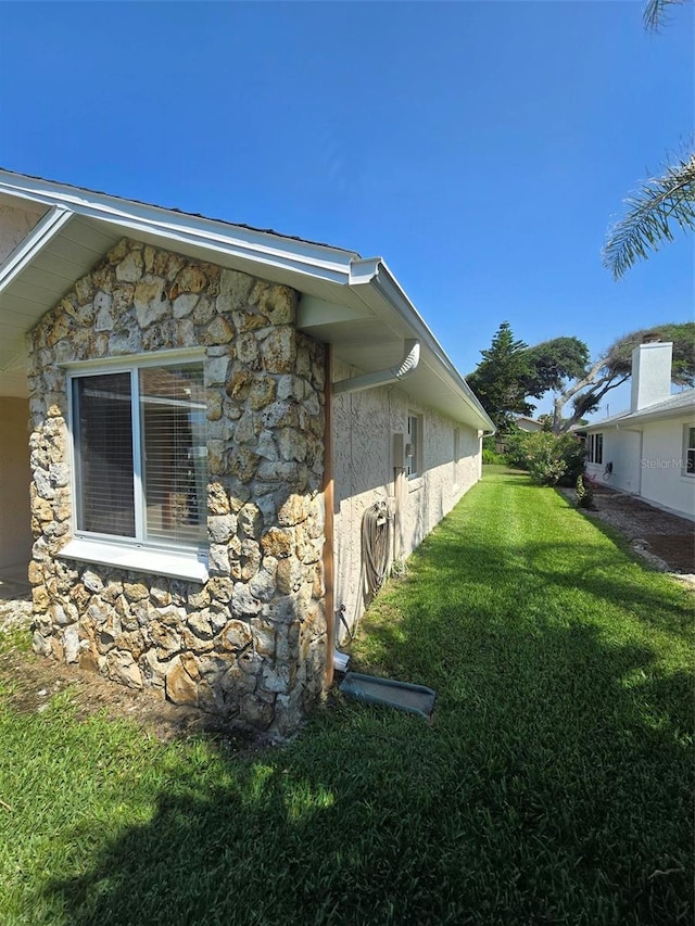 view of side of home with stucco siding, stone siding, and a lawn