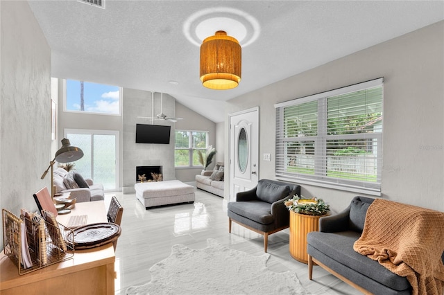 living room with a wealth of natural light, a large fireplace, ceiling fan, and a textured ceiling