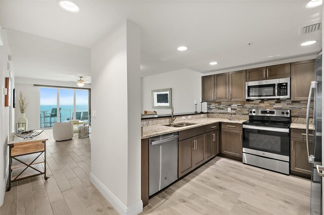 kitchen featuring light stone countertops, backsplash, stainless steel appliances, sink, and light hardwood / wood-style flooring