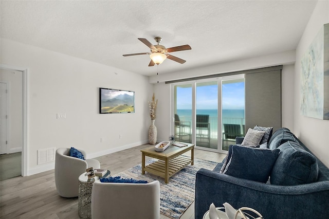 living room featuring ceiling fan, light hardwood / wood-style floors, a water view, and a textured ceiling