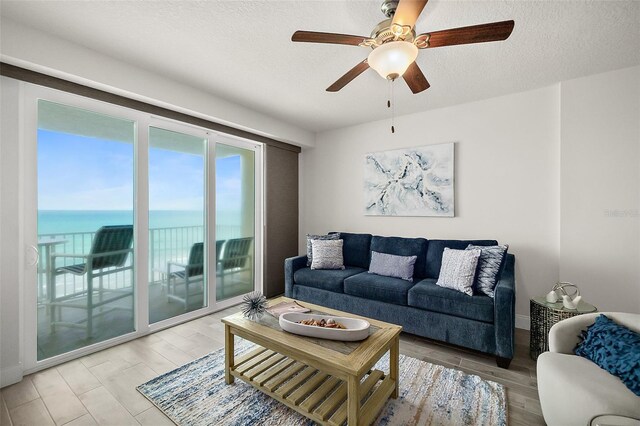 living room featuring wood-type flooring, a textured ceiling, a water view, and ceiling fan