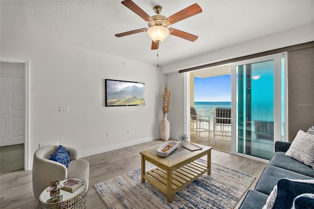 living room with ceiling fan, light hardwood / wood-style flooring, a water view, and a textured ceiling