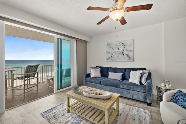 living room featuring a textured ceiling, a water view, and ceiling fan