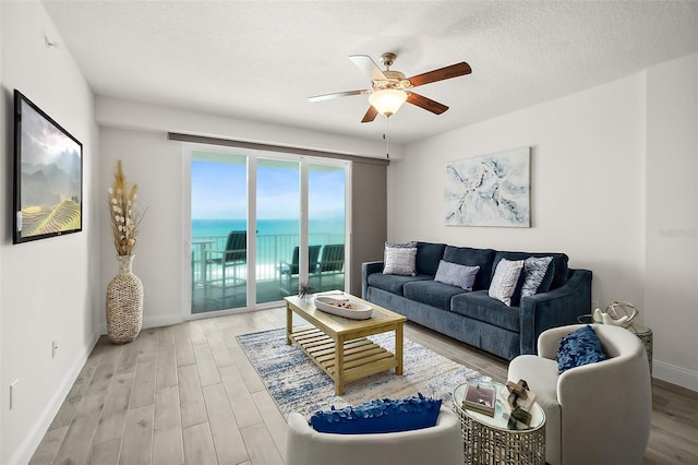 living room featuring ceiling fan, a water view, a textured ceiling, and hardwood / wood-style flooring