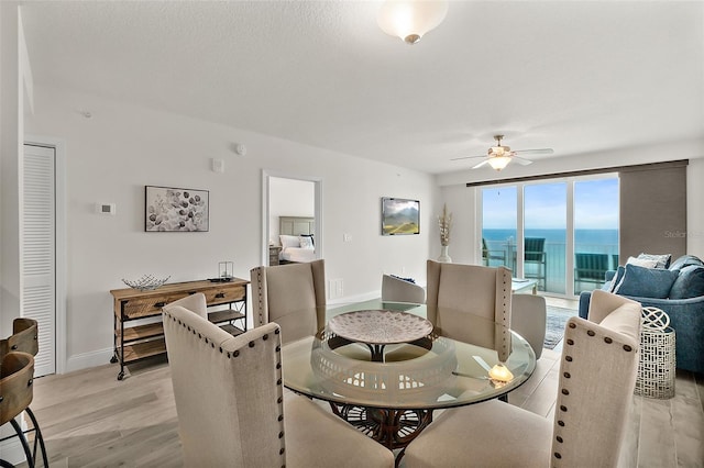 dining space with a water view, light hardwood / wood-style flooring, and ceiling fan