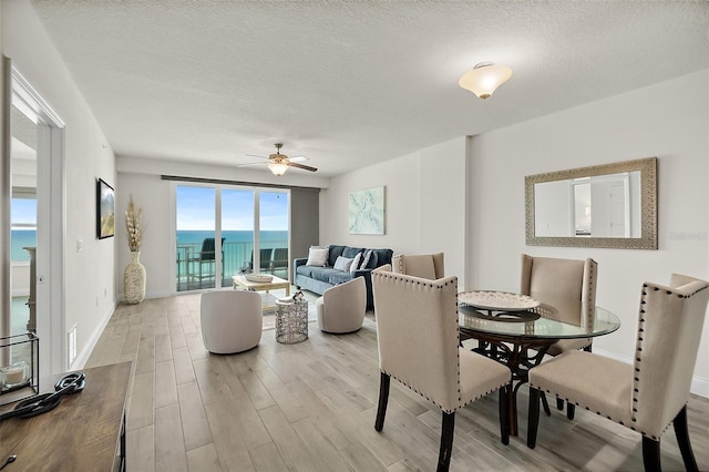 dining space with ceiling fan, a water view, light hardwood / wood-style floors, and a textured ceiling