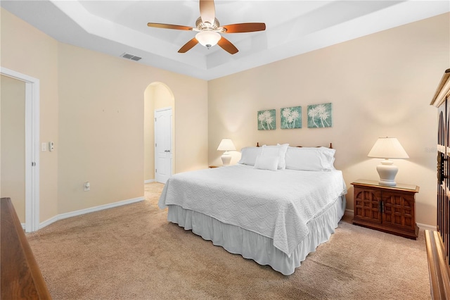 bedroom featuring a raised ceiling, ceiling fan, and light carpet