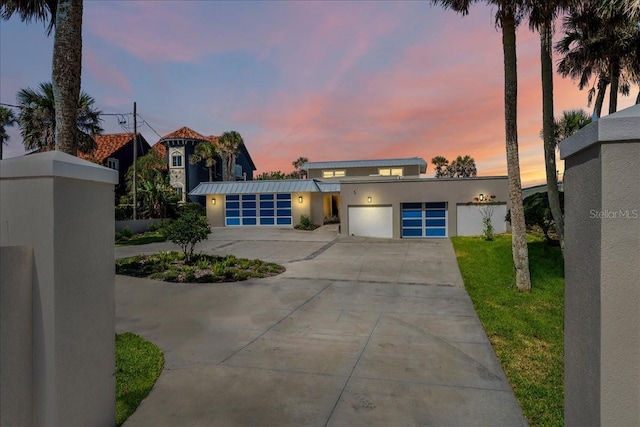 view of front of property with a garage, concrete driveway, metal roof, a standing seam roof, and stucco siding