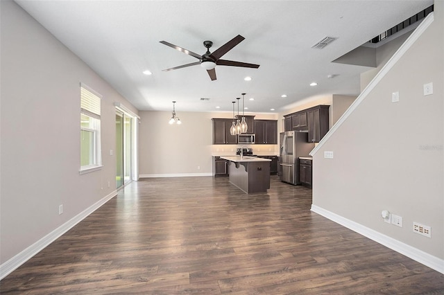 kitchen featuring a kitchen bar, appliances with stainless steel finishes, decorative light fixtures, a kitchen island with sink, and dark brown cabinetry