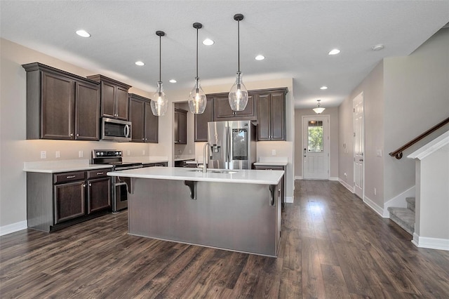 kitchen with a center island with sink, stainless steel appliances, decorative light fixtures, dark brown cabinets, and a breakfast bar