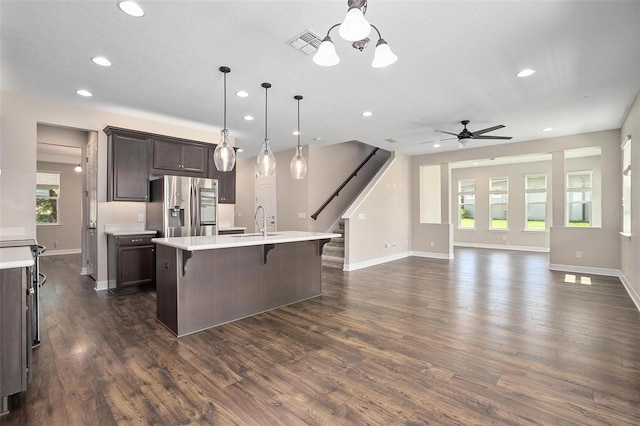 kitchen featuring a kitchen bar, hanging light fixtures, stainless steel fridge, a kitchen island with sink, and dark brown cabinets