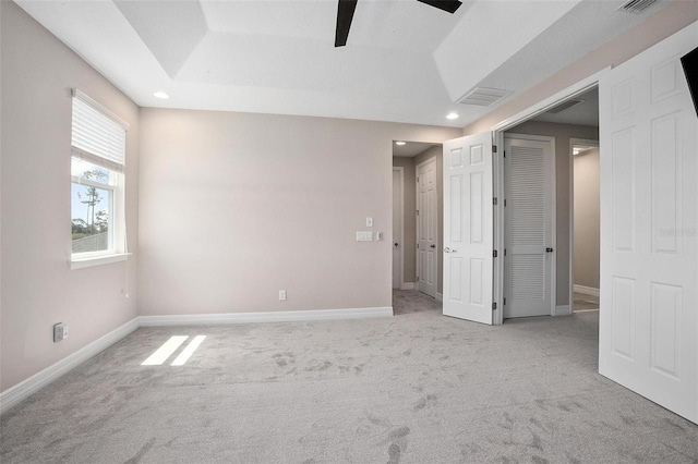 unfurnished bedroom with light carpet, ceiling fan, and a tray ceiling