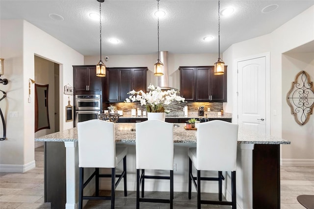 kitchen featuring decorative backsplash, pendant lighting, a center island with sink, and a breakfast bar area