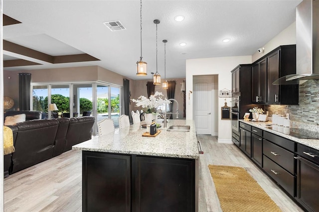 kitchen featuring black electric stovetop, wall chimney range hood, sink, a large island, and light hardwood / wood-style floors