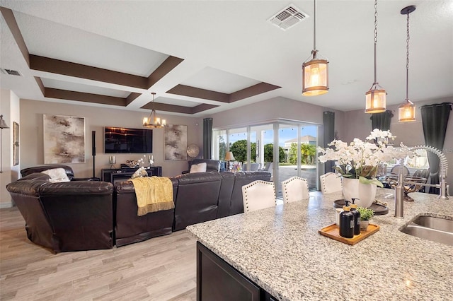 kitchen featuring a chandelier, coffered ceiling, pendant lighting, and light stone counters