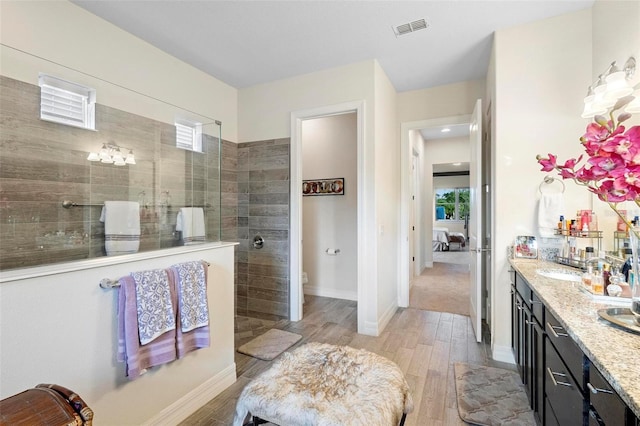 bathroom with hardwood / wood-style floors, vanity, toilet, and a tile shower