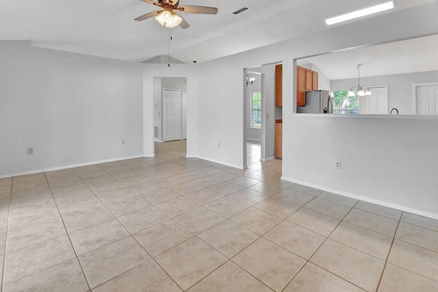 empty room with vaulted ceiling, light tile patterned floors, and ceiling fan with notable chandelier