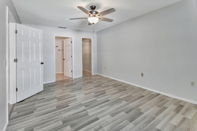 unfurnished bedroom featuring a walk in closet, ceiling fan, a textured ceiling, light hardwood / wood-style floors, and a closet