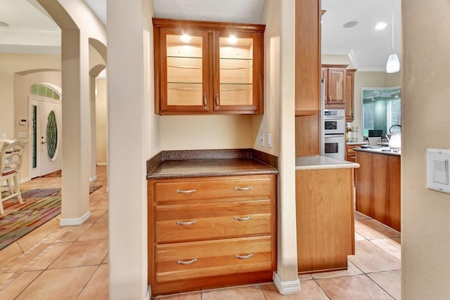 kitchen with light stone counters, white double oven, hanging light fixtures, crown molding, and light tile floors