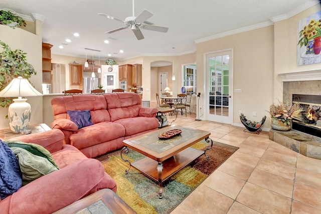 tiled living room with ceiling fan, a fireplace, and ornamental molding