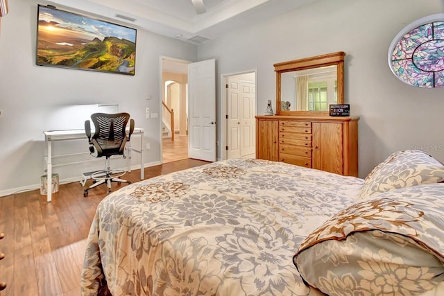 bedroom with wood-type flooring, ceiling fan, and a tray ceiling