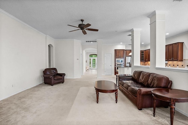 living room featuring ceiling fan, decorative columns, a textured ceiling, light carpet, and ornamental molding