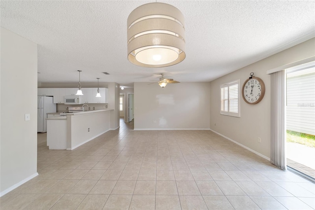 unfurnished living room featuring a textured ceiling, ceiling fan, light tile patterned floors, and sink