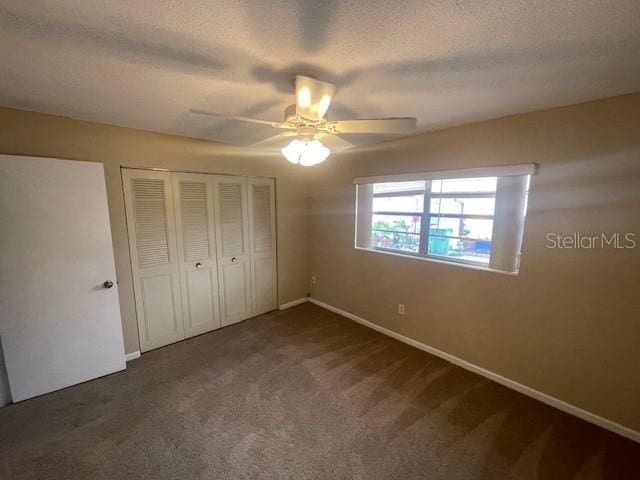 unfurnished bedroom with ceiling fan, a textured ceiling, a closet, and dark colored carpet