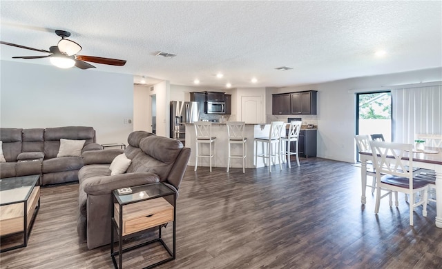 living room with a textured ceiling, dark wood-type flooring, and ceiling fan