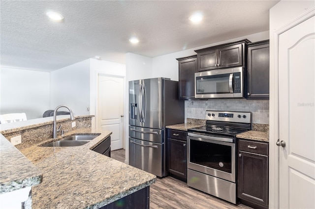 kitchen featuring a center island with sink, stainless steel appliances, decorative backsplash, light hardwood / wood-style flooring, and sink