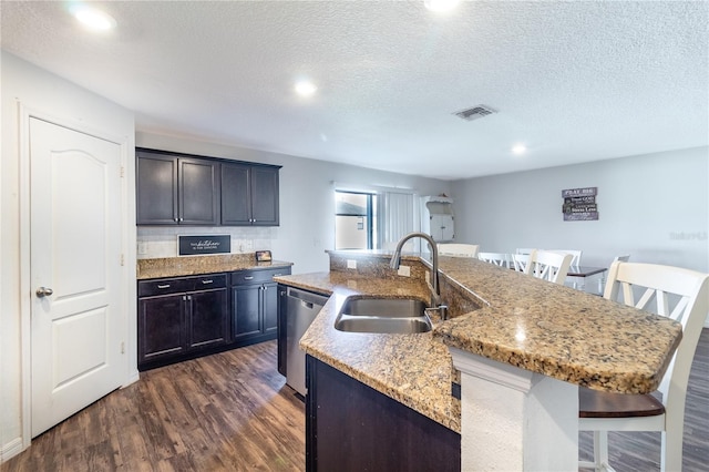 kitchen with a textured ceiling, dishwasher, sink, a center island with sink, and a breakfast bar area