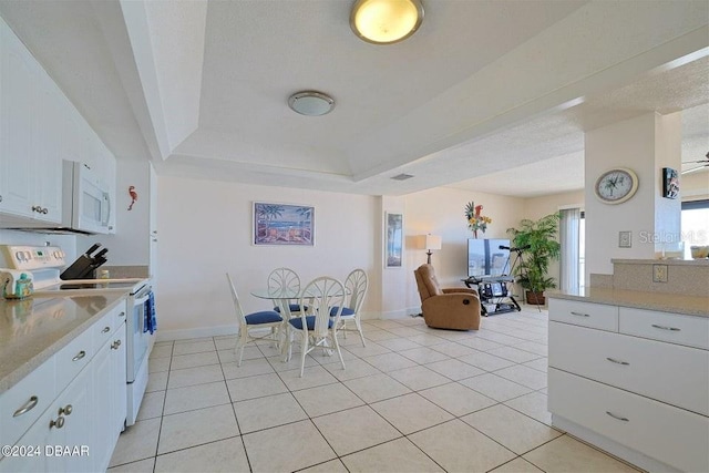 kitchen with a tray ceiling, white cabinetry, light tile patterned flooring, and white appliances