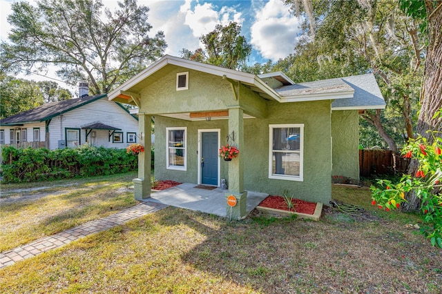 bungalow featuring a front lawn, roof with shingles, fence, and stucco siding