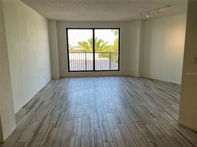 empty room featuring rail lighting, a textured ceiling, and hardwood / wood-style floors