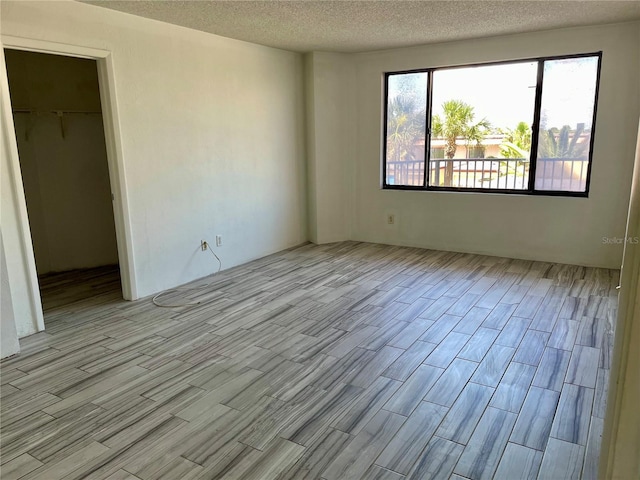 unfurnished bedroom featuring light hardwood / wood-style flooring, a closet, a textured ceiling, and a walk in closet