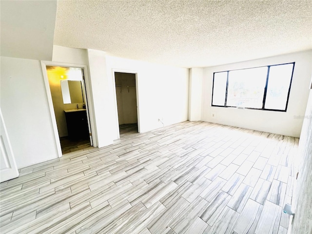 unfurnished bedroom featuring a spacious closet, a textured ceiling, ensuite bath, and a closet