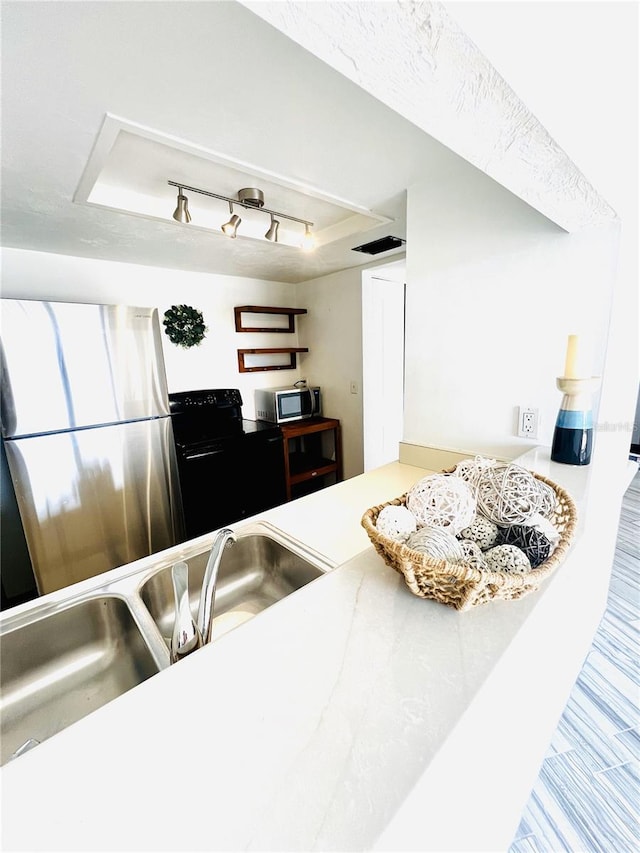 kitchen with rail lighting, appliances with stainless steel finishes, sink, and a tray ceiling