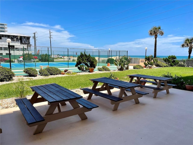 view of property's community featuring a water view, a lawn, and tennis court