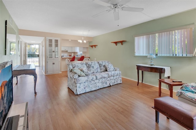 living room with ceiling fan with notable chandelier, baseboards, and light wood-style floors