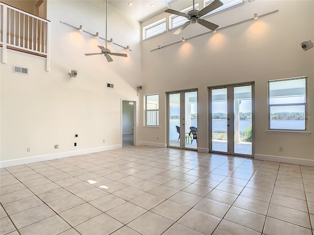 tiled spare room featuring a high ceiling, ceiling fan, a water view, and french doors