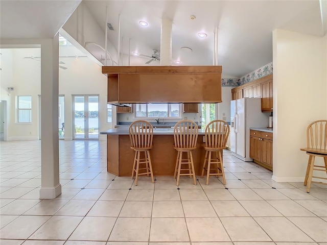 kitchen featuring white refrigerator with ice dispenser, a kitchen breakfast bar, kitchen peninsula, ceiling fan, and light tile patterned floors