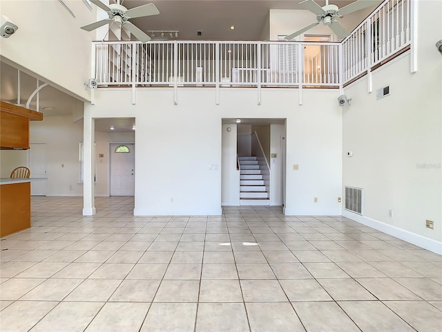 unfurnished living room featuring ceiling fan, light tile patterned floors, and a towering ceiling