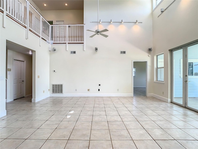 unfurnished living room with ceiling fan, a wealth of natural light, light tile patterned floors, and a towering ceiling