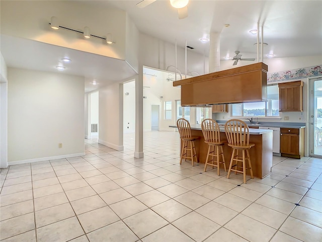 kitchen featuring ceiling fan, dishwasher, a kitchen island, a kitchen bar, and light tile patterned floors