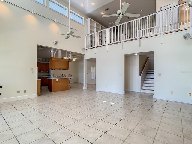 unfurnished living room with ceiling fan, a towering ceiling, and light tile patterned flooring