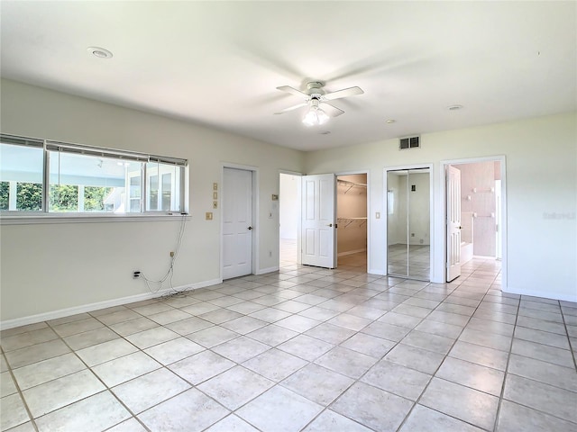 unfurnished bedroom featuring a spacious closet, light tile patterned floors, ensuite bathroom, ceiling fan, and a closet